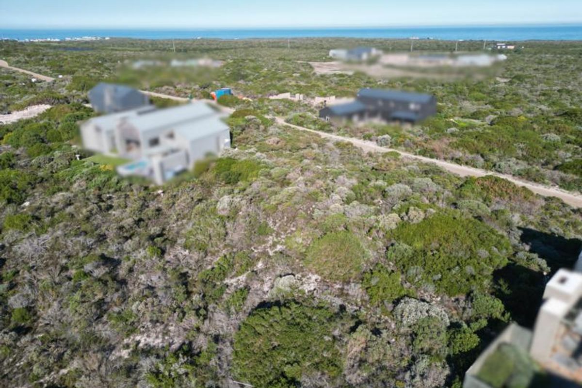 An aerial view of a vacant residential plot featuring native coastal vegetation and access to a nearby unpaved road.
