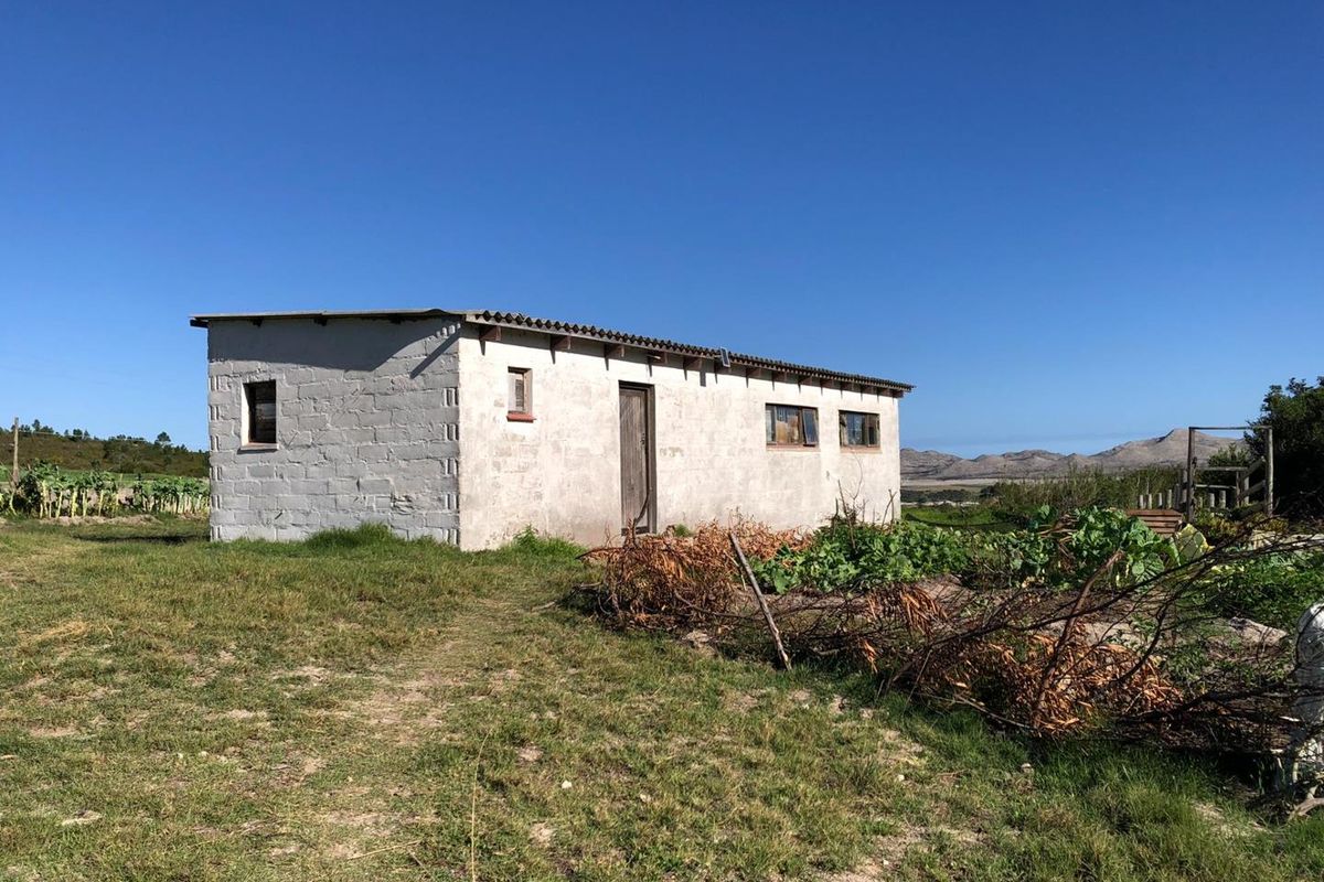 A detached outbuilding on a farm property featuring concrete block construction, a corrugated roof, and surrounding garden space with mountain views.