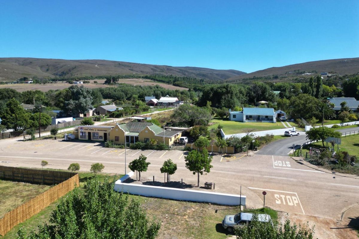 Aerial view of a commercial property featuring a paved parking area, boundary walls, and surrounding landscape in a rural setting.