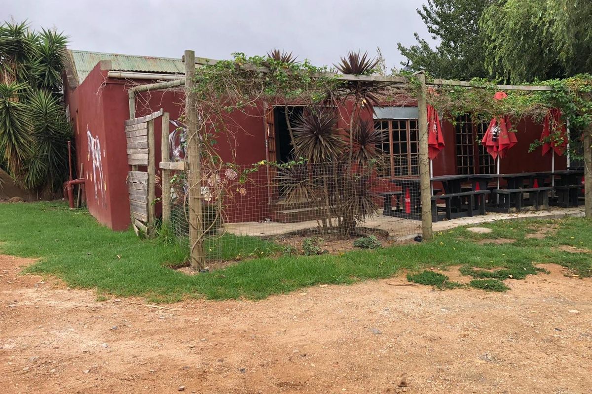 Rear exterior view of a commercial building featuring a timber pergola, concrete patio area, and weathered facade finishes.