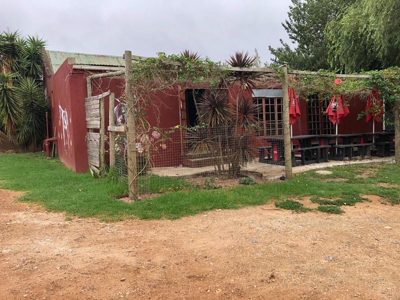 Rear exterior view of a commercial building featuring a timber pergola, concrete patio area, and weathered facade finishes.