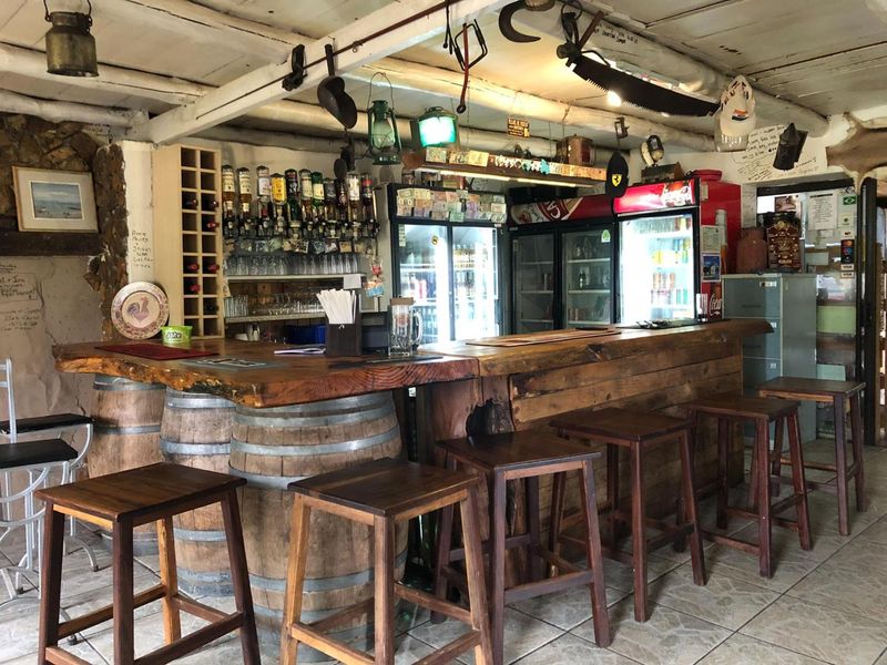 Rustic commercial bar area featuring a custom timber counter, built-in wine storage, and commercial refrigeration units under exposed timber ceiling beams.