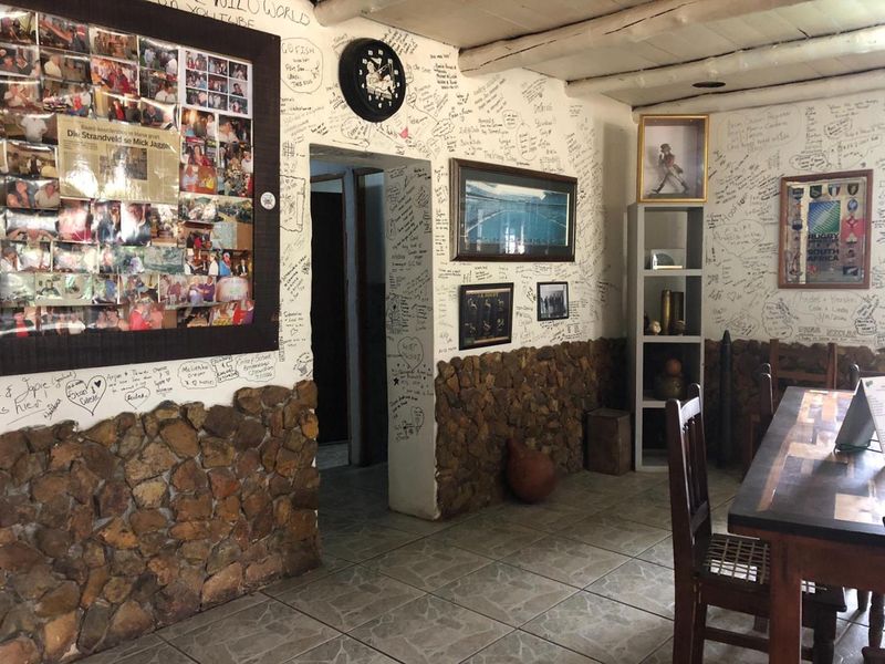 Dining area featuring rustic stone wall cladding, ceramic floor tiles, and exposed beam ceilings, currently decorated with extensive wall writing.