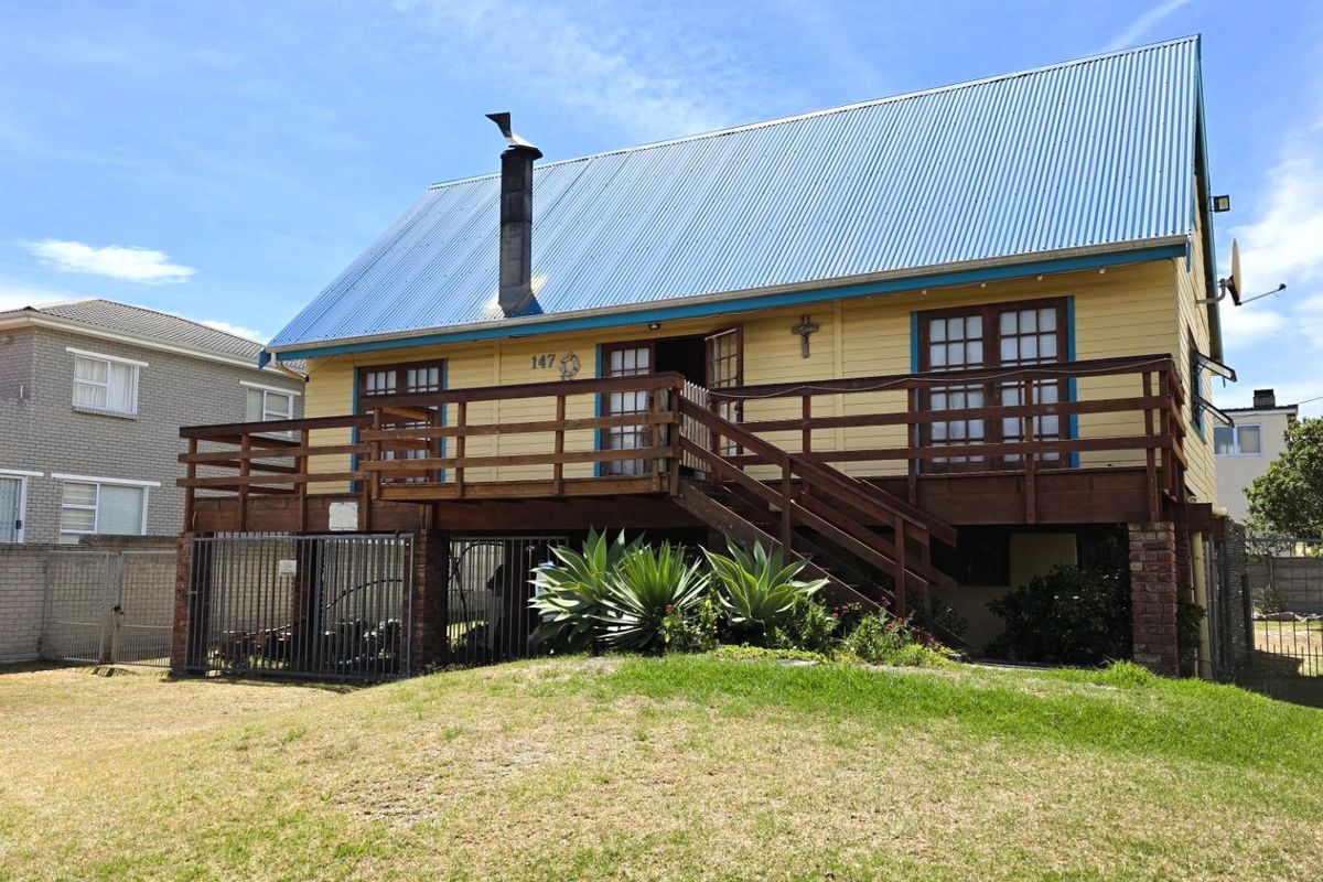 Rear view of a two-story house featuring a raised timber deck, corrugated metal roof, and timber cladding with a surrounding garden area.