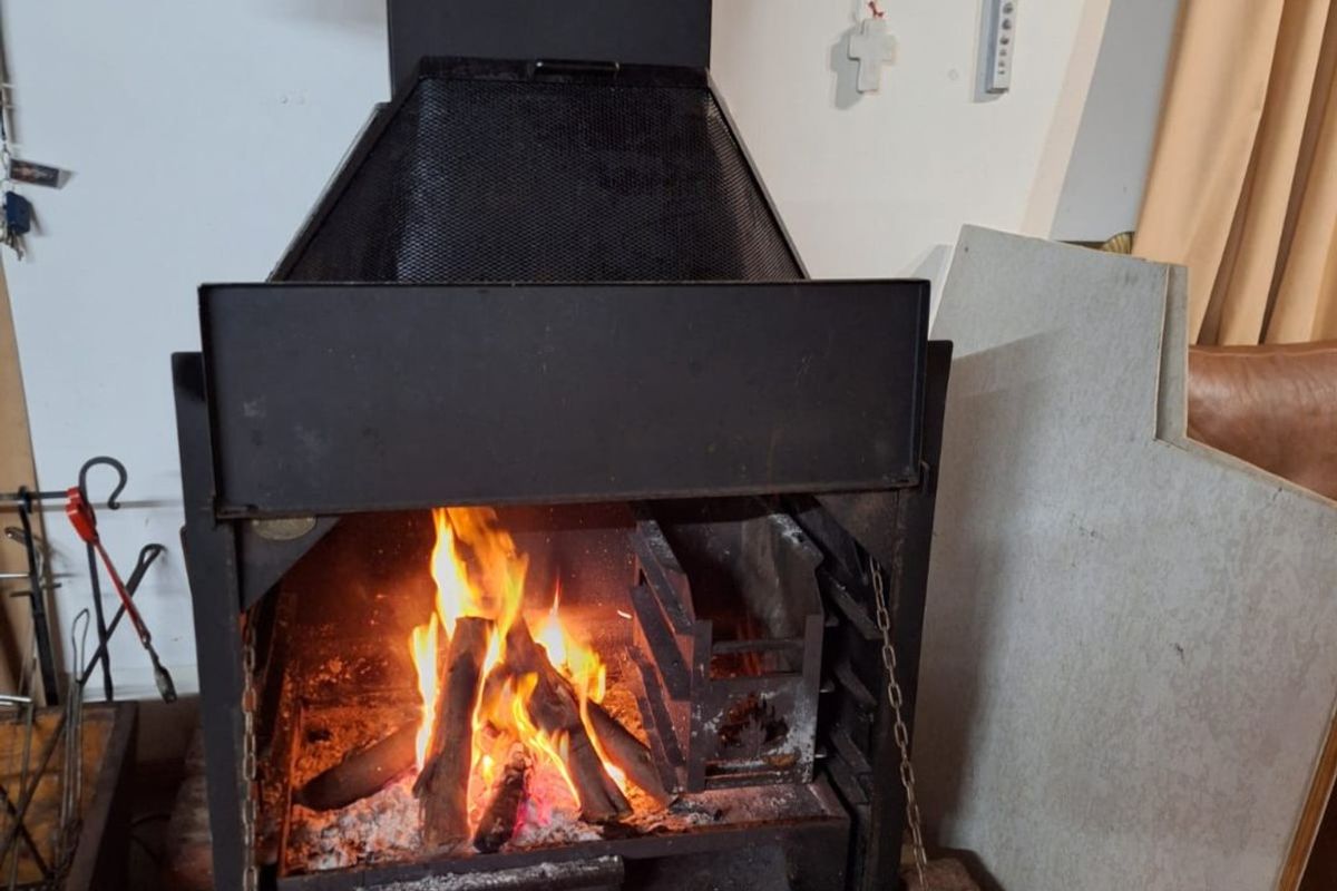 A functional indoor built-in metal fireplace with a burning wood fire, featuring a brick hearth and integrated chimney hood.