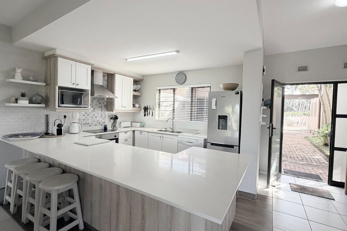 Modern kitchen featuring quartz countertops, a breakfast bar, built-in cabinetry, and a tiled backsplash, with direct access to an outdoor patio area.