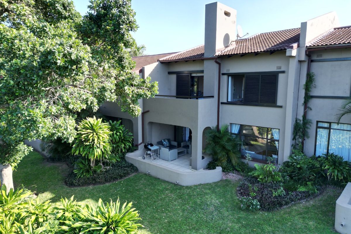 Rear view of the townhouse featuring a covered patio, upper balcony, chimney, and well-maintained landscaped garden area.