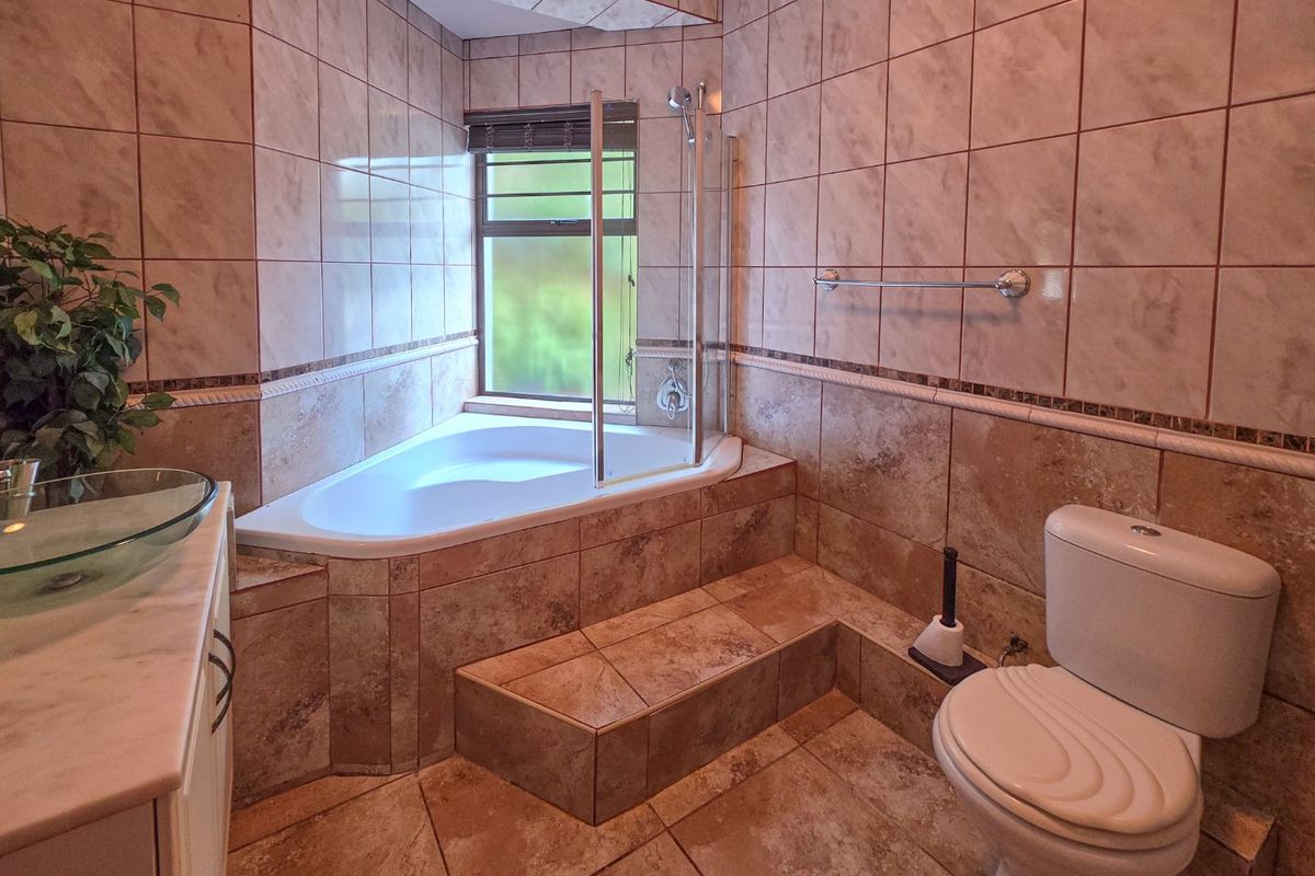 A tiled bathroom featuring a corner bathtub with a glass shower screen, a toilet, and a vanity area.