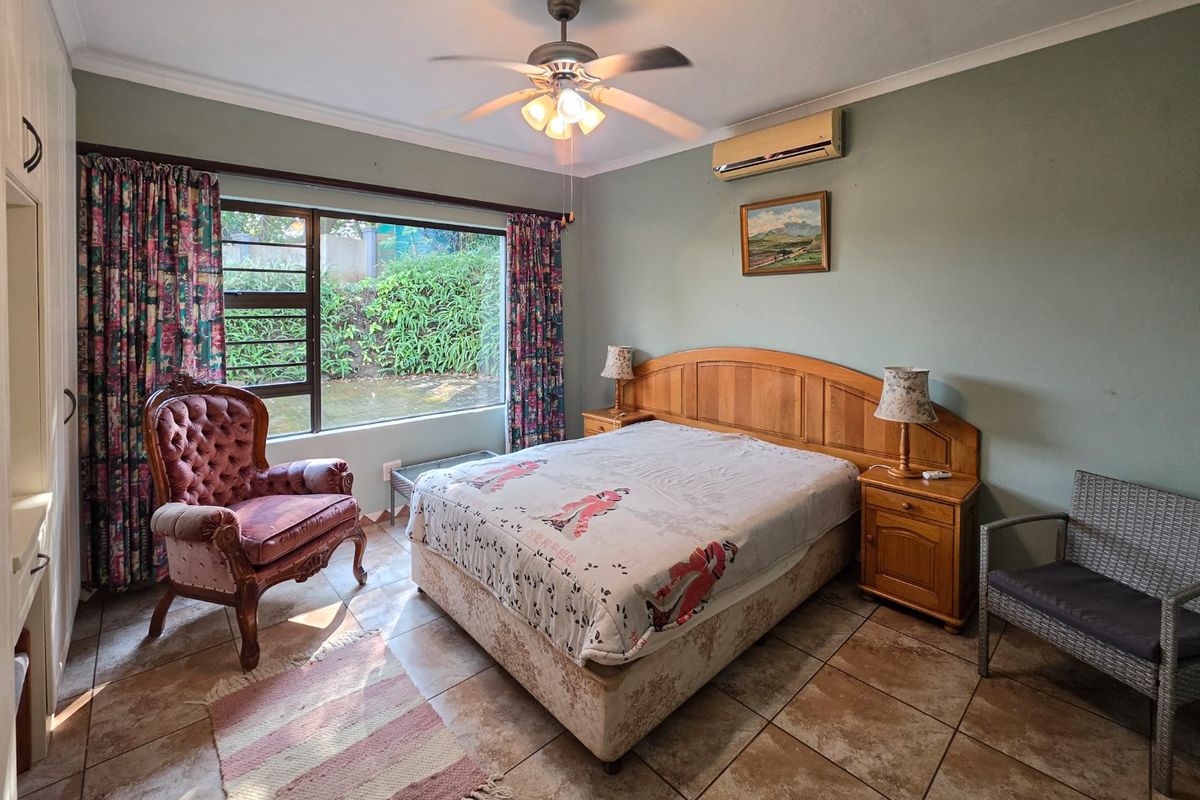 A spacious bedroom featuring tiled flooring, a ceiling fan, and a wall-mounted air conditioning unit, offering a comfortable and functional living space.