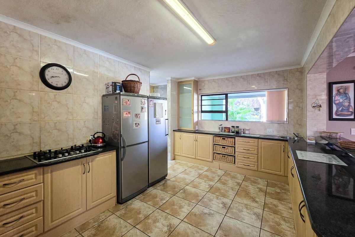 A functional kitchen featuring granite countertops, gas hob, tiled splashbacks, and ample built-in cabinetry with tiled flooring throughout.