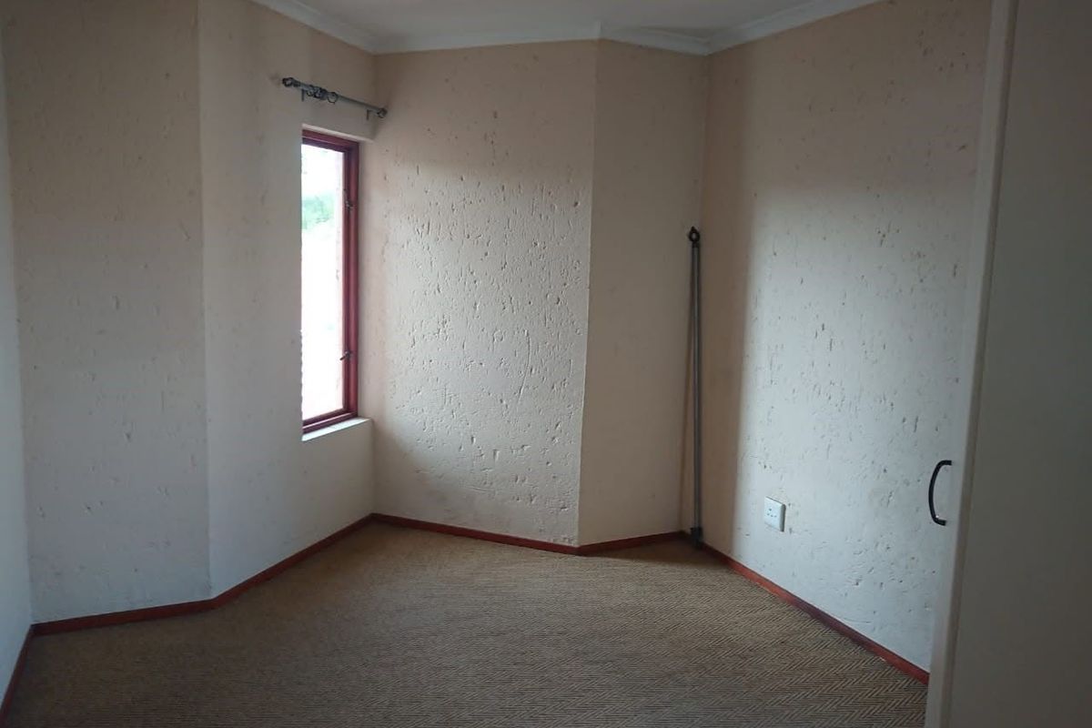 An empty bedroom featuring textured walls, carpet flooring, and a single window, offering a blank canvas for personalization.