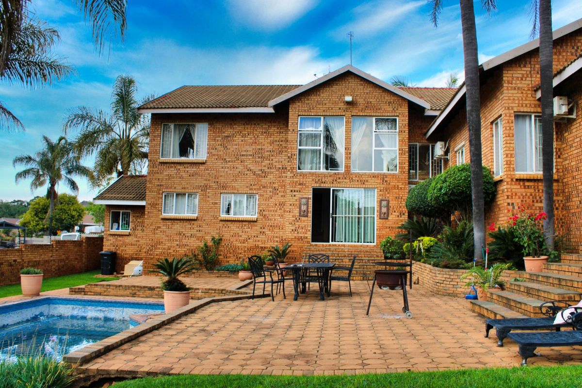 Rear view of a double-story facebrick house featuring a paved patio area, swimming pool, and established garden landscaping.