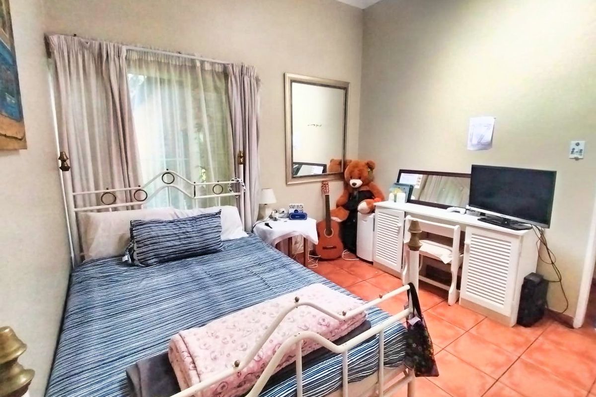 A bedroom featuring terracotta floor tiles and a window with curtain treatments.