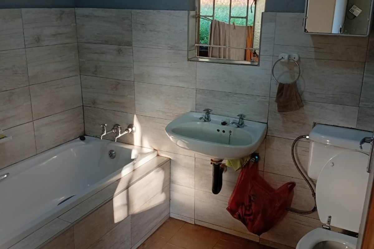 A functional bathroom featuring a built-in bathtub, wall-mounted basin, and toilet with tiled wall finishes and a window with security bars.