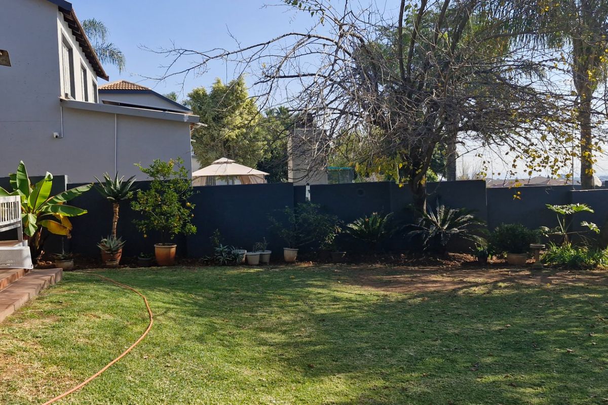Rear garden view featuring a tiled patio, sliding glass doors, and a private perimeter boundary wall with established trees and lawn.
