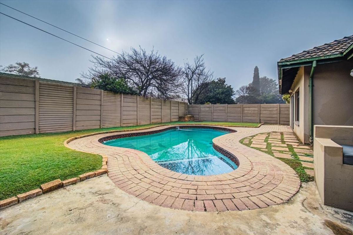 Outdoor pool area featuring a kidney-shaped swimming pool, brick paving, and a precast concrete boundary wall in a private backyard setting.