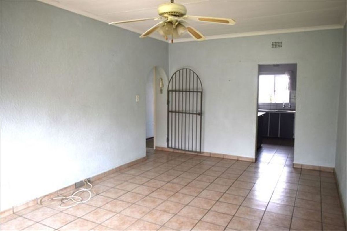 An empty living room featuring tiled flooring, a ceiling fan, and an arched doorway leading to the kitchen area.