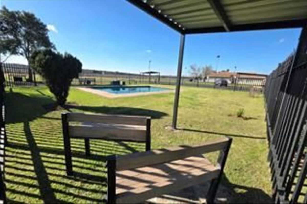 Outdoor pool area featuring a covered patio space, lawn, and perimeter fencing, providing a communal recreational area.