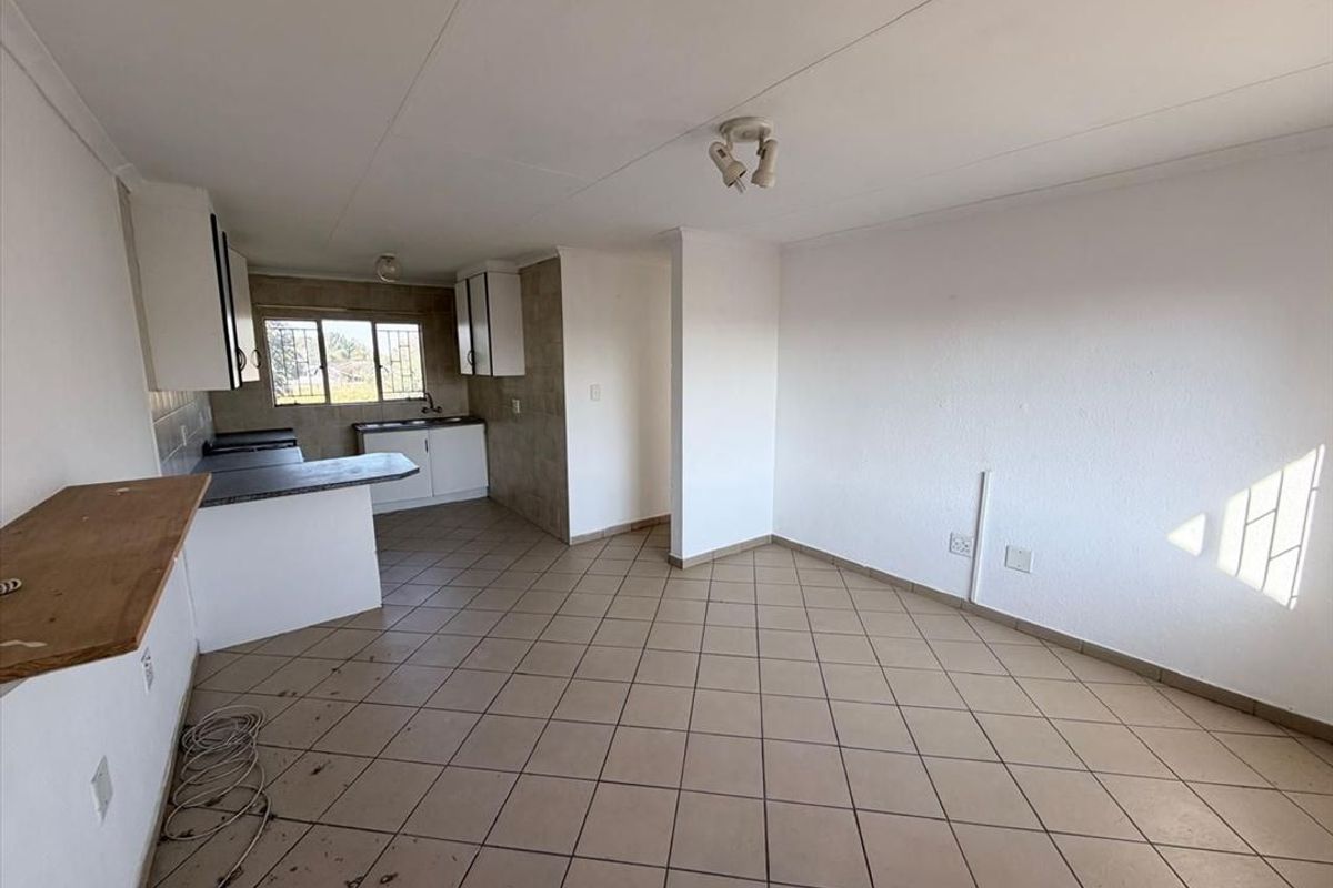 An open-plan living and kitchen area featuring tiled flooring, built-in cabinetry, and a breakfast counter, offering a blank canvas for renovation.