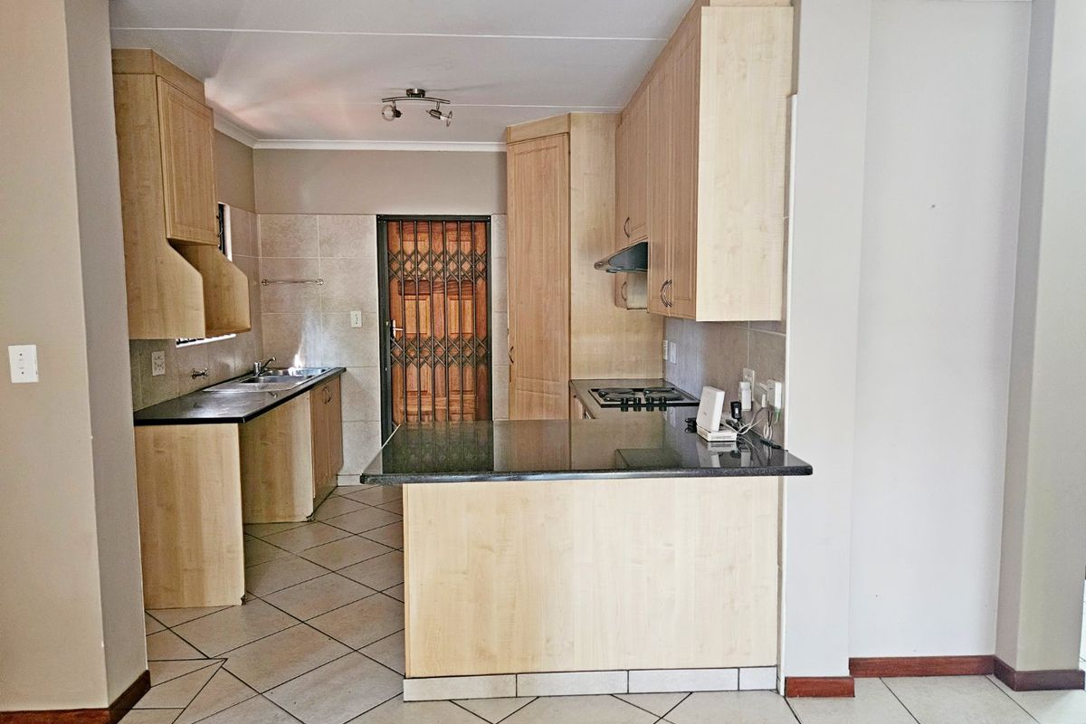 A functional kitchen featuring light wood cabinetry, granite countertops, a gas hob with extractor fan, and tiled flooring, leading to a secure exterior door.