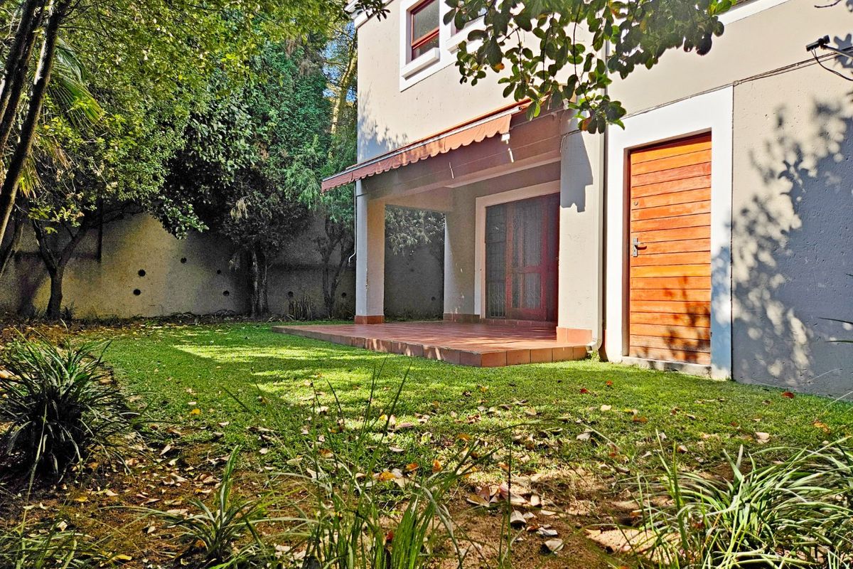 Rear view of the townhouse featuring a covered patio with tiled flooring, a retractable awning, and a private garden with a boundary wall.
