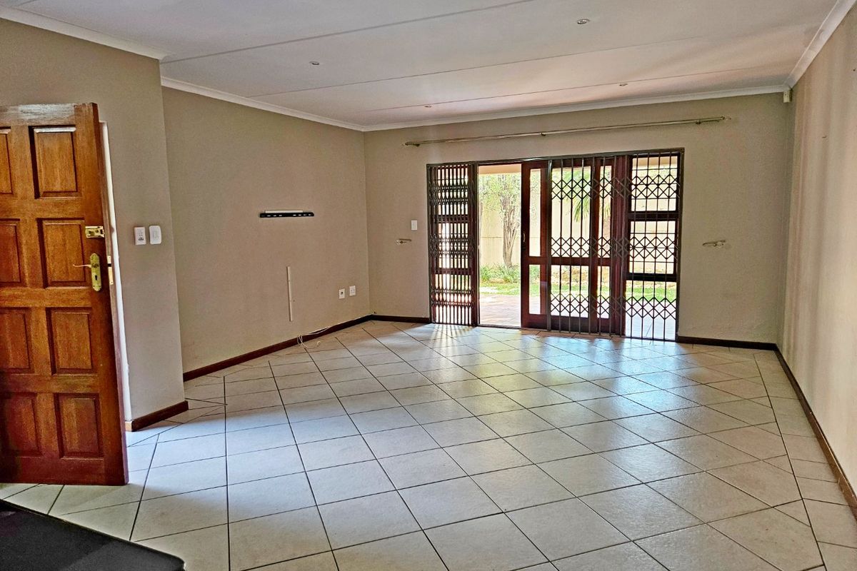 Spacious, empty living area featuring neutral tiled flooring, recessed lighting, and sliding glass doors with security gates leading to the outdoor space.