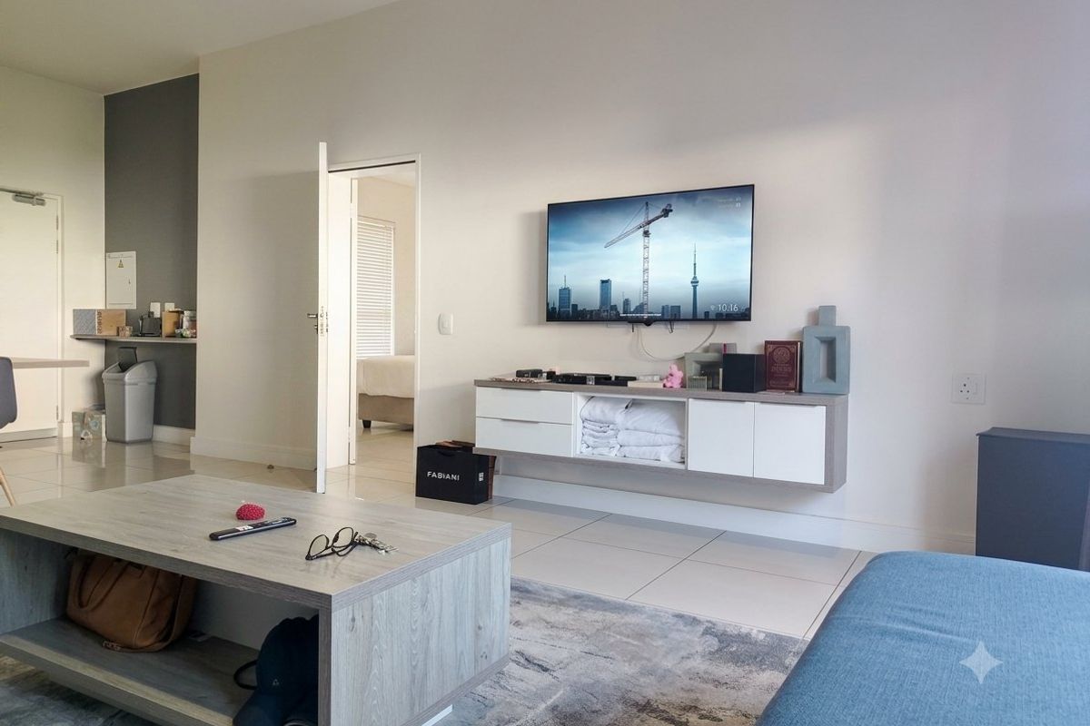A modern living room featuring tiled flooring, a wall-mounted media console, and neutral wall finishes, providing a clean and functional living space.