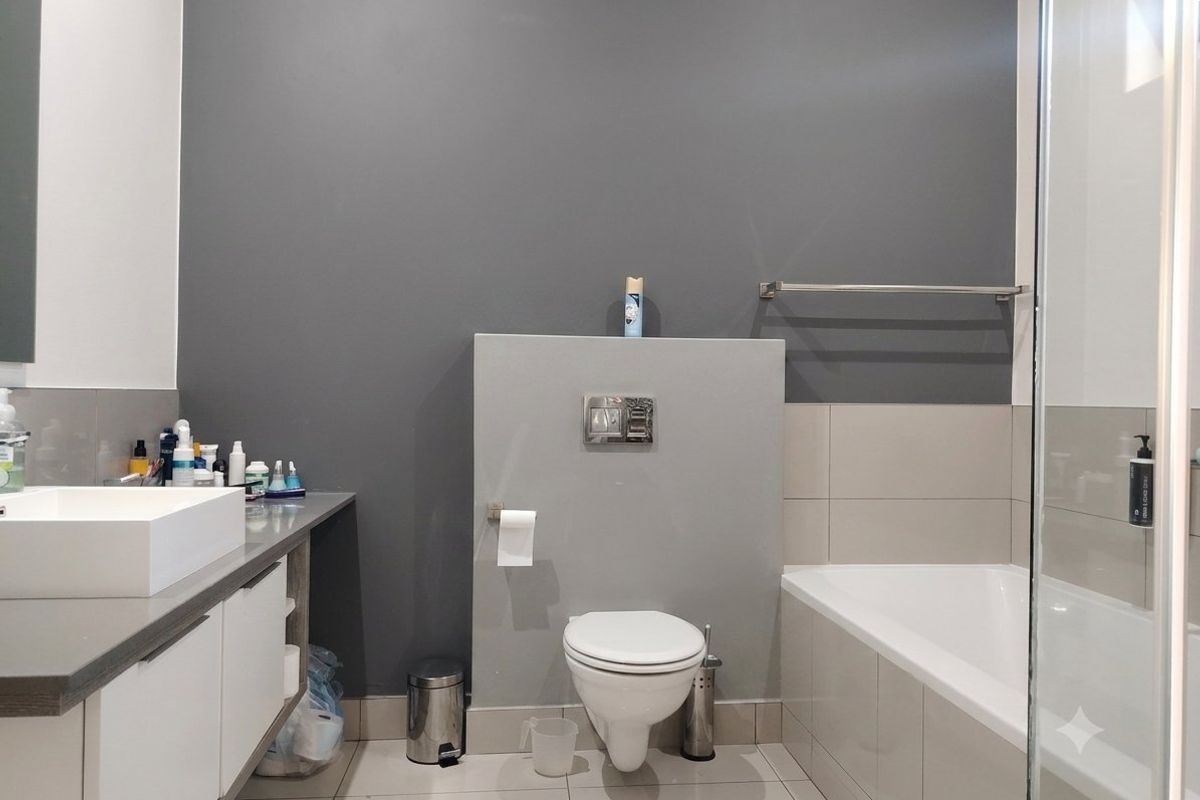 Modern bathroom featuring a wall-hung toilet with concealed cistern, vanity cabinet with countertop basin, bathtub, and a glass shower screen.