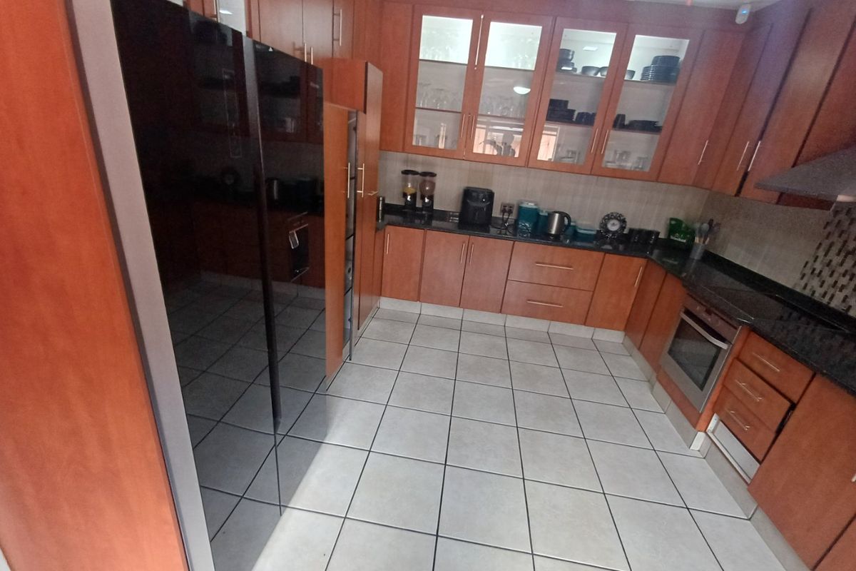 A functional kitchen featuring warm-toned wooden cabinetry, granite countertops, built-in oven, extractor fan, and tiled flooring with ample storage space.