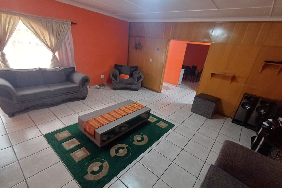 A living room featuring tiled flooring and wood paneling, with an adjacent dining area visible through the doorway.