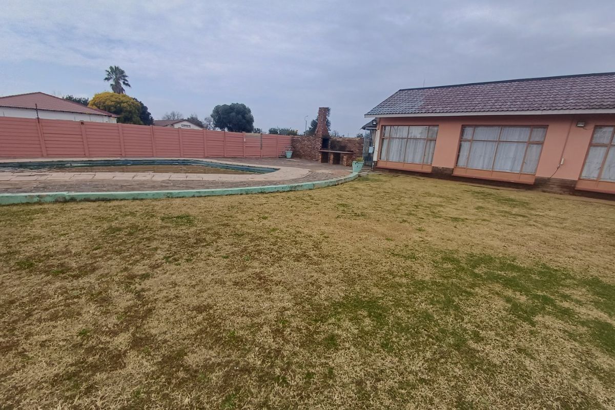 Rear garden area featuring a swimming pool, brick braai, and perimeter walling, adjacent to the main house structure.