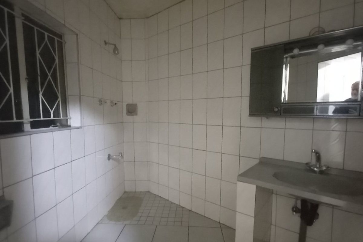 A dated bathroom featuring full-height wall tiling, a built-in vanity with an integrated sink, and a shower area with security bars on the window.