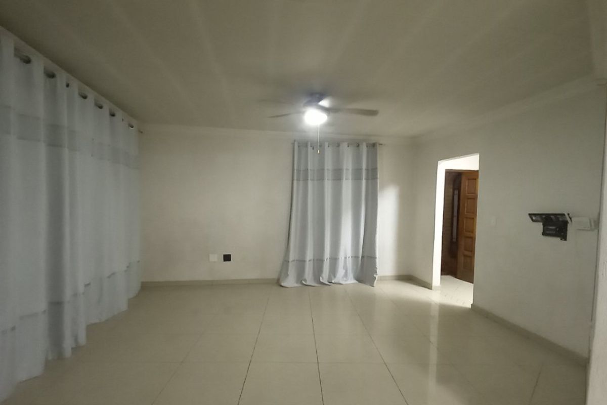 A spacious, empty living room featuring neutral tiled flooring, a ceiling fan, and coved ceilings, providing a blank canvas for interior design.