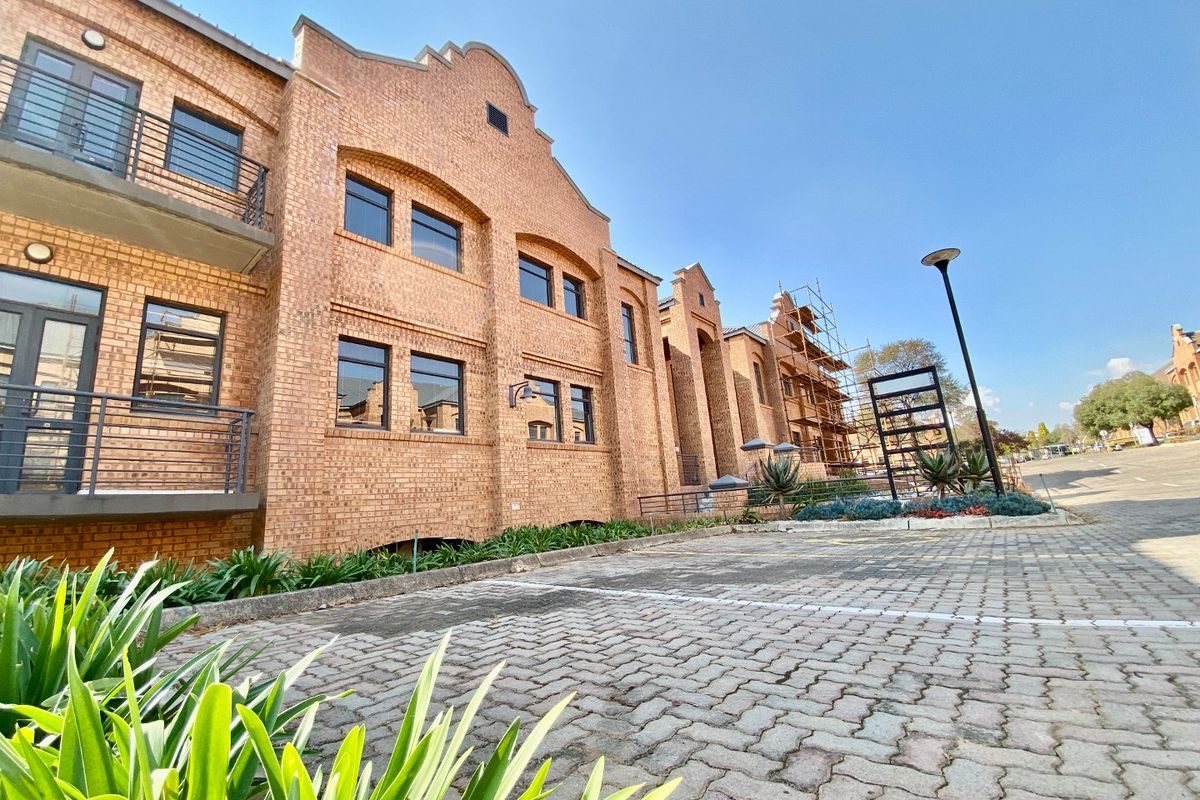 A low-angle view of a commercial face brick building featuring balconies, paved parking area, and ongoing maintenance work with scaffolding visible.