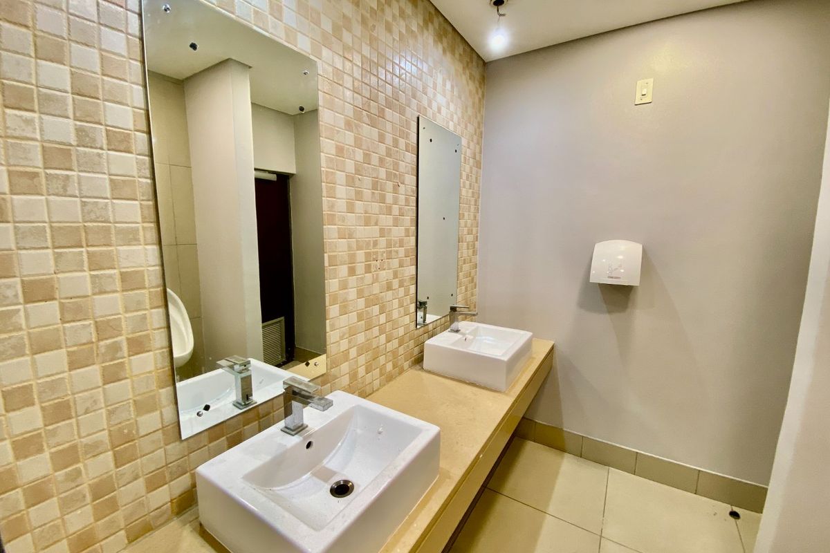 A clean commercial bathroom featuring dual vessel sinks, chrome faucets, mosaic tiled walls, and wall-mounted mirrors.