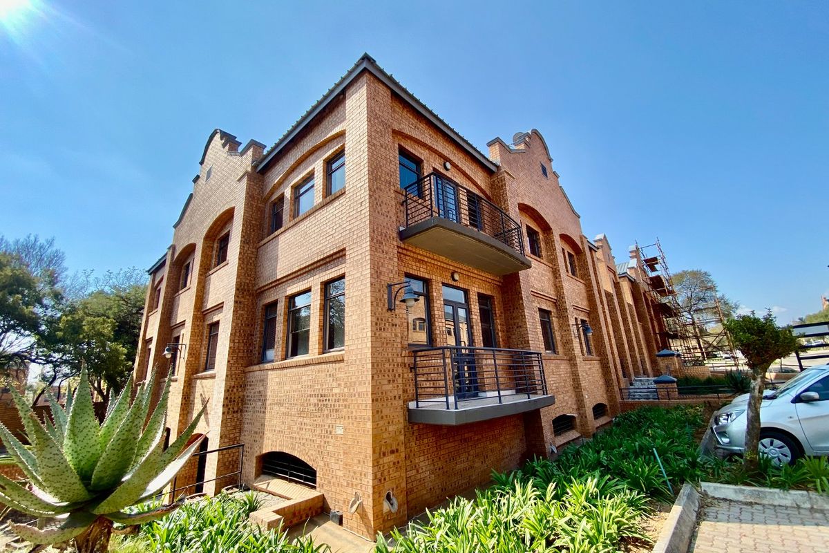 A multi-story commercial building featuring a classic face brick facade, gabled architectural details, and integrated metal balconies.