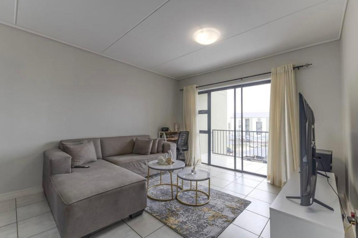 A bright living room featuring tiled flooring and a large sliding glass door providing direct access to a private balcony.