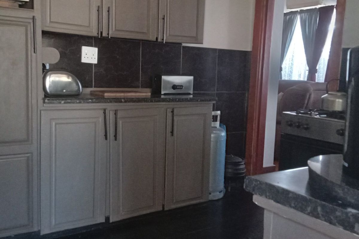 A functional kitchen featuring grey built-in cabinetry, dark tiled backsplash, and laminate countertops with an integrated gas stove.