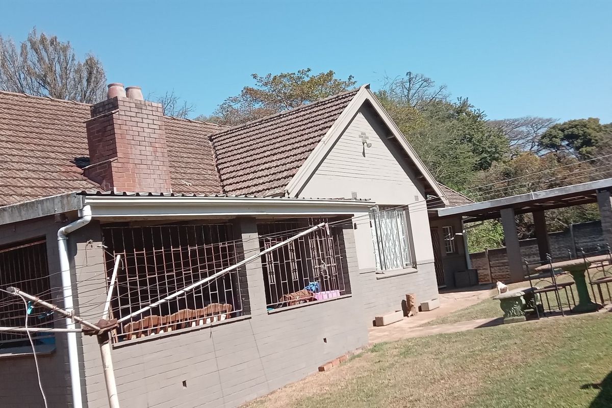 Rear view of the house featuring a tiled roof, brick chimney, covered patio area with security bars, and an adjacent carport structure.