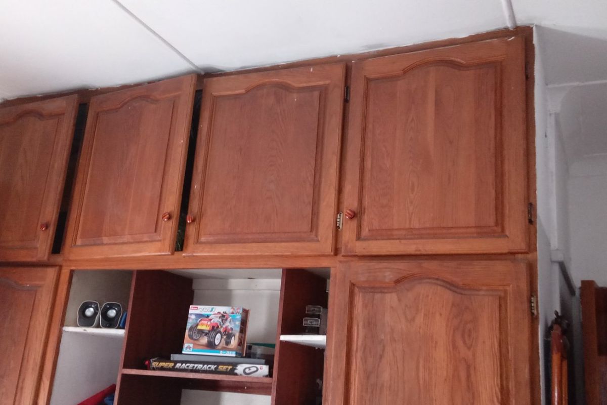 Bedroom featuring dated wooden built-in cupboards with overhead storage units and ceiling cornice detailing.