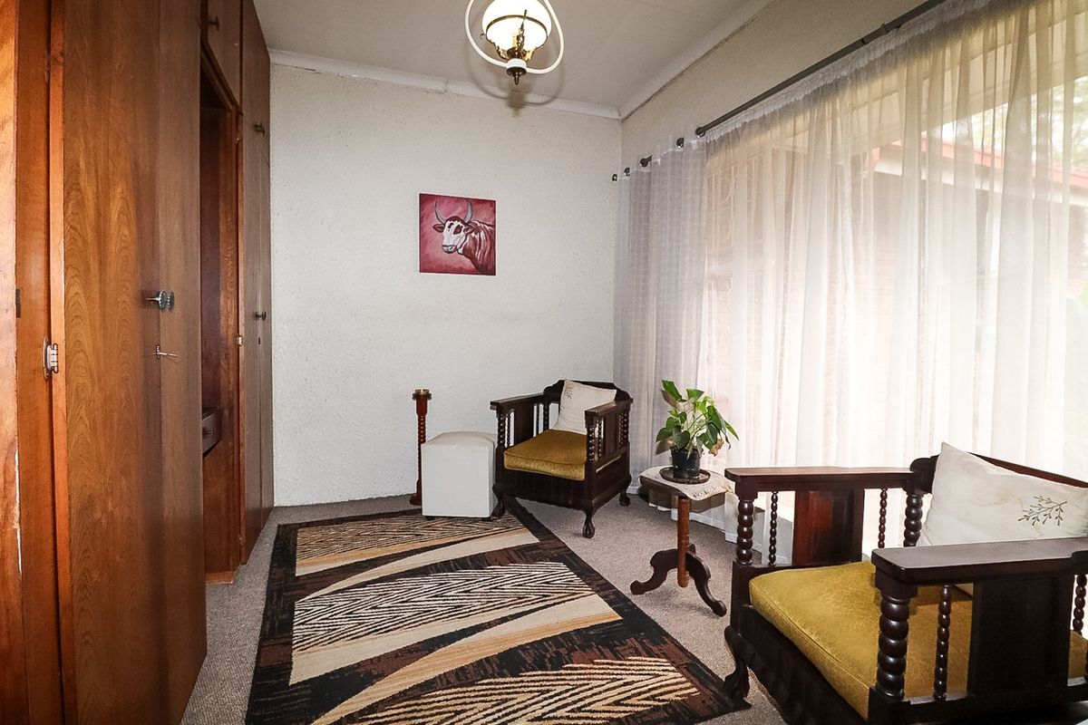 A bedroom featuring built-in wooden cupboards, carpeted flooring, and a large window with curtains, offering a dated but functional living space.
