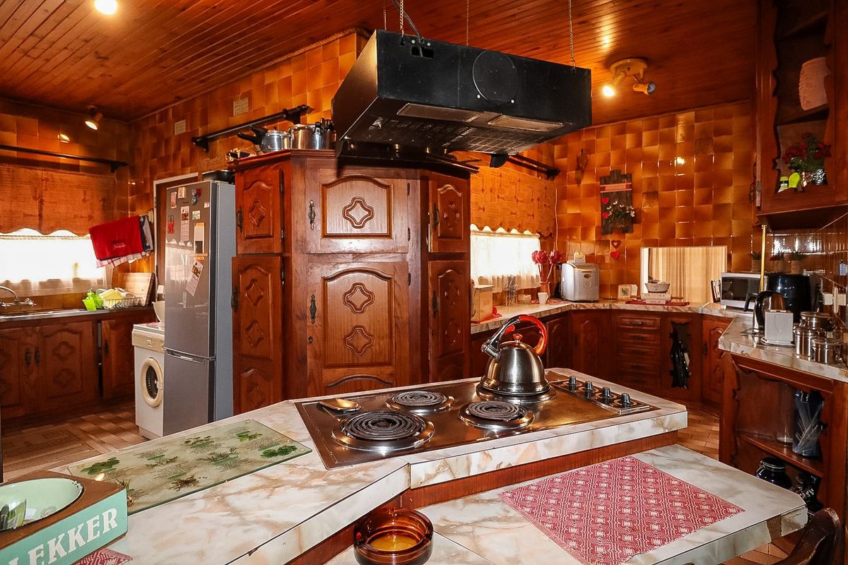 A traditional kitchen featuring extensive wooden cabinetry, marble-look countertops, an integrated electric hob with extractor fan, and a warm timber-paneled ceiling.