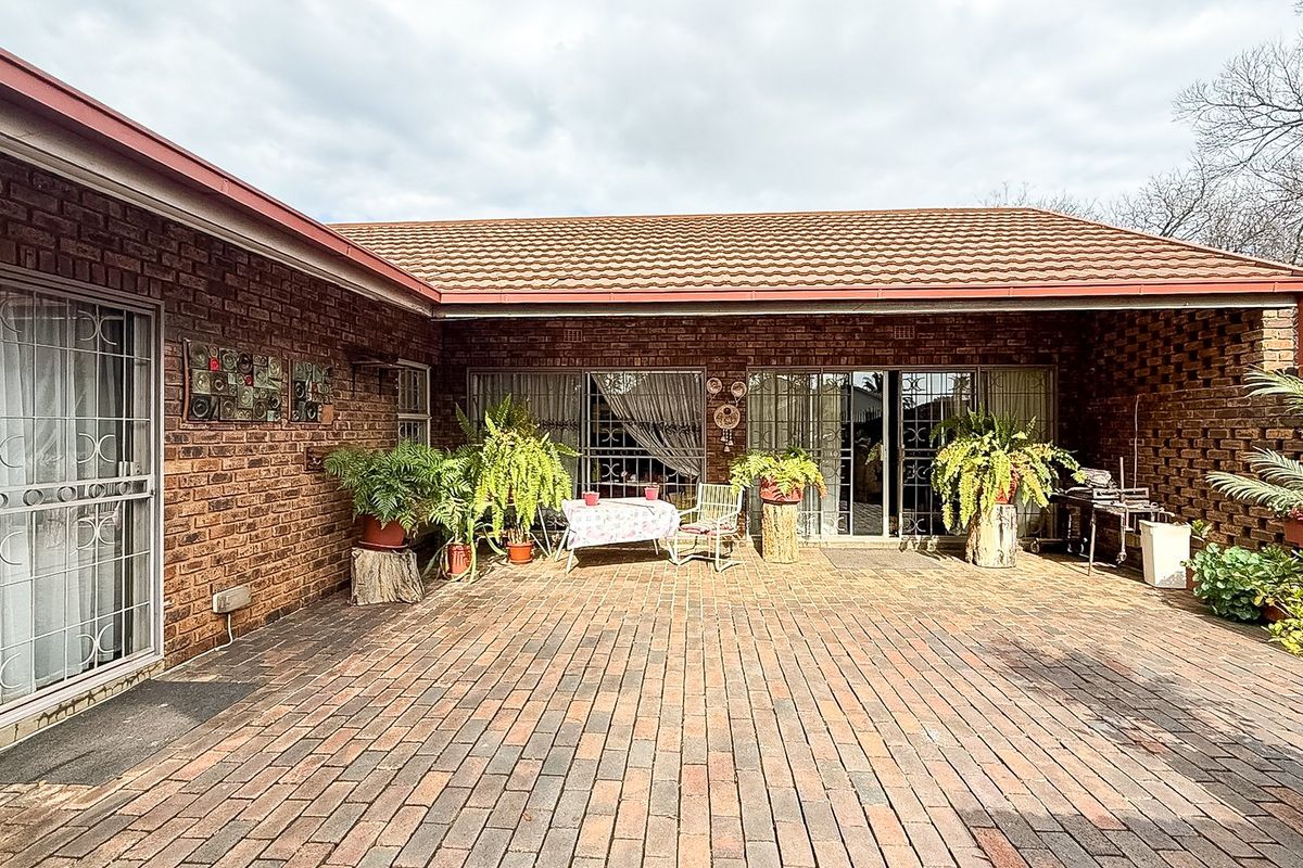 A spacious rear patio featuring brick paving, face brick walls, and multiple sliding glass door access points to the home.