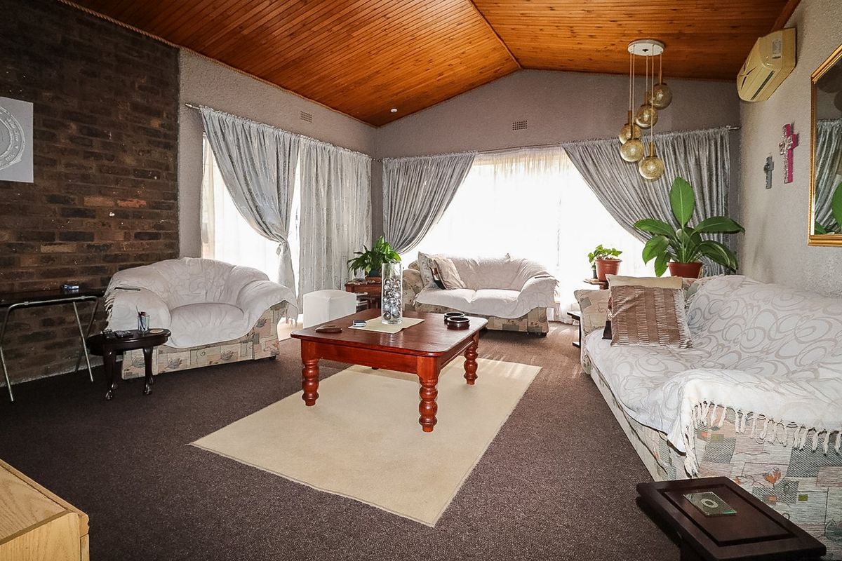 Spacious living room featuring a vaulted timber ceiling, exposed brick feature wall, and split system air conditioning.