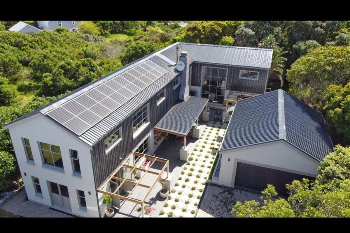 Aerial view of a modern two-story residence featuring a metal roof with integrated solar panels, a detached garage, and a landscaped courtyard.