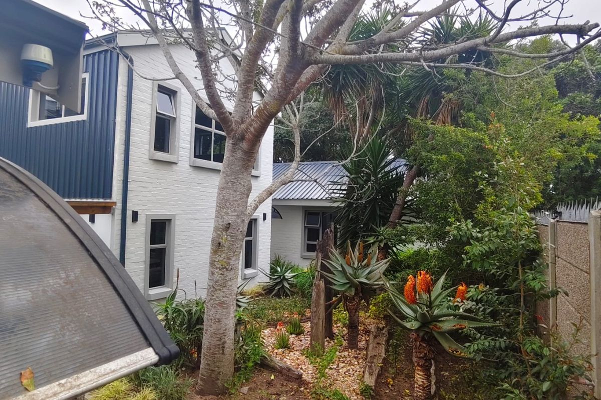 Rear view of the property featuring a combination of painted brick and metal cladding with established garden landscaping.