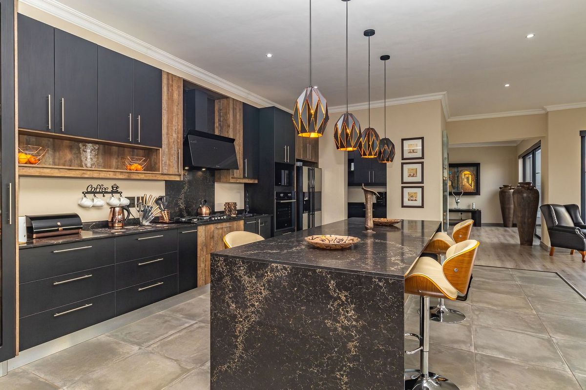 Modern kitchen featuring dark cabinetry, a large stone island, integrated appliances, and stylish pendant lighting, seamlessly flowing into the adjacent living area.