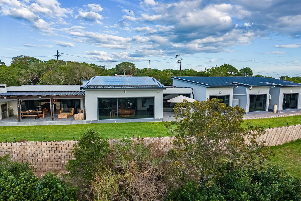 Aerial view of the rear elevation featuring a modern farmhouse design with solar panels, a covered patio with built-in braai, and landscaped grounds.