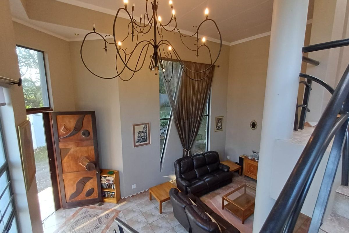 Spacious living area featuring high ceilings, a decorative wrought iron chandelier, tiled flooring, and a unique feature front door with natural light.