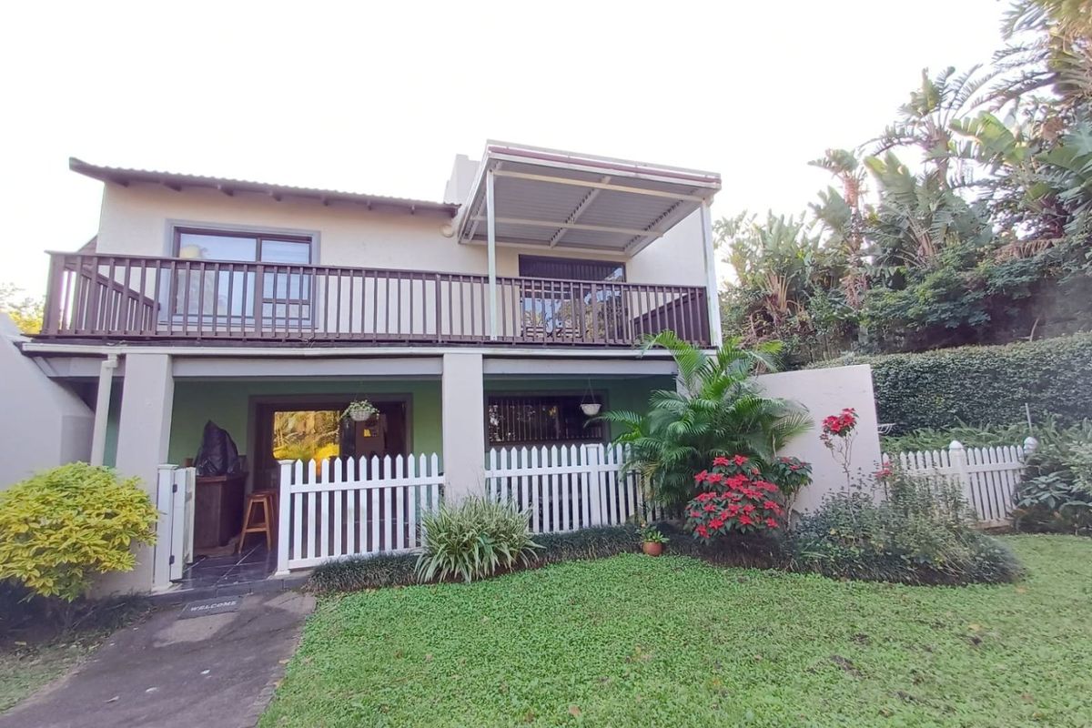 Rear view of the house featuring a covered ground-floor patio, an upper-level balcony with timber railing, and a well-maintained garden with picket fencing.